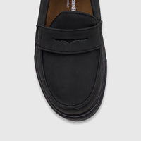 Close-up of a single black casual slip-on shoe for boys, featuring a penny loafer strap and a chunky ridged sole.