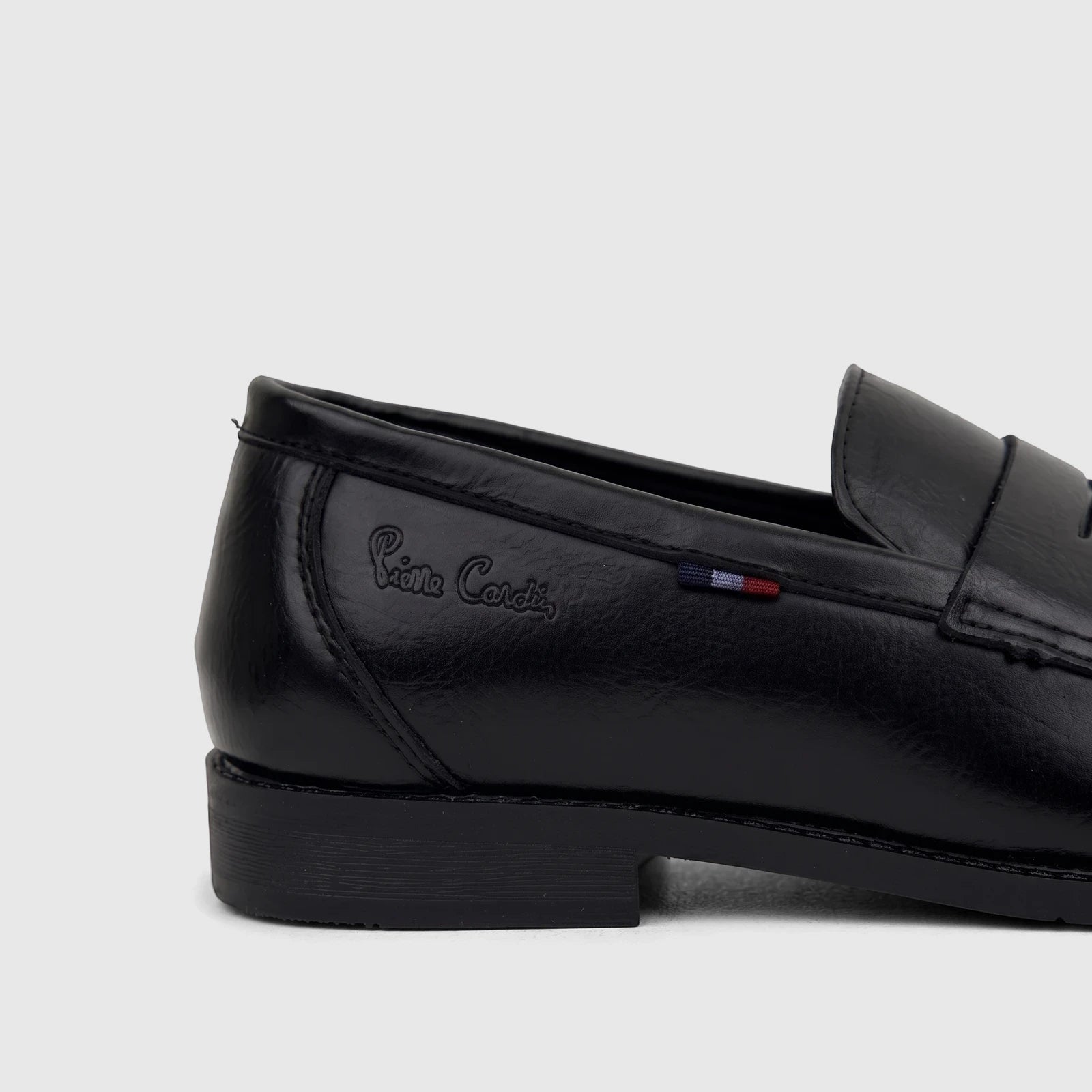 Side view of a black Pierre Cardin youth slip-on dress loafer shoe, featuring a shiny finish and a subtle striped detail.
