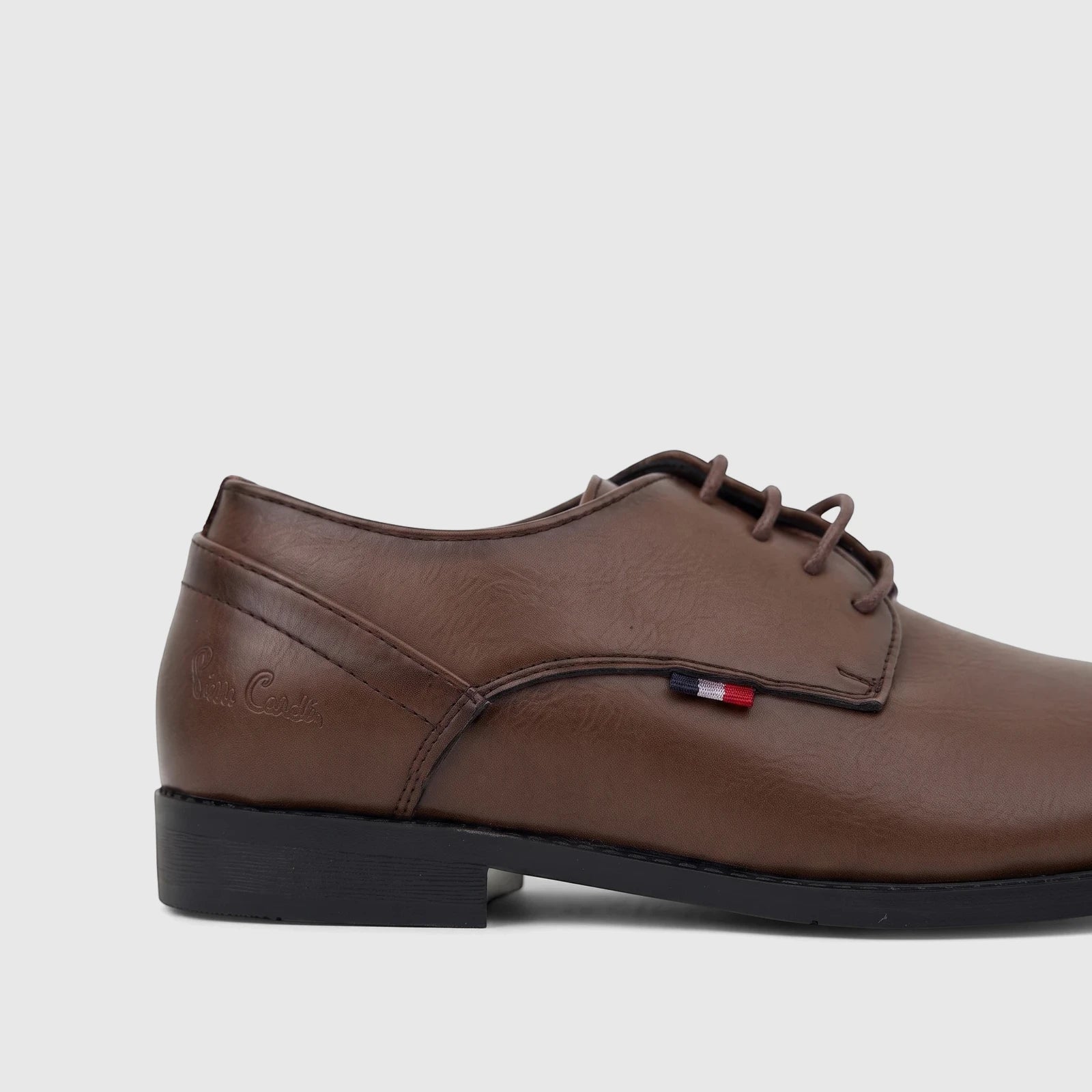 Brown faux leather lace-up dress shoe for youth, featuring a classic design and a distinctive red, white, and blue tag