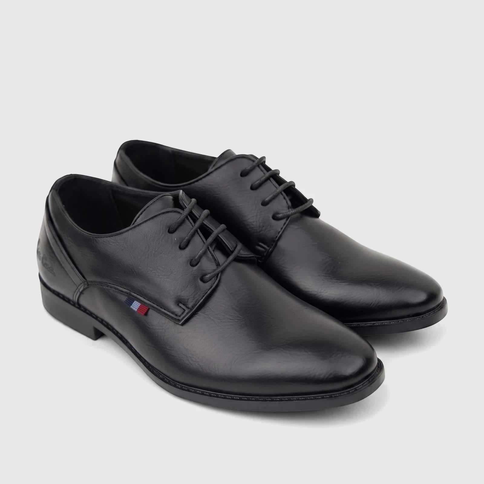 A pair of black lace-up dress shoes for boys, made of leather, displayed with a small red, white, and blue detail.