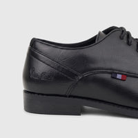 Black PC Boys Youth lace-up dress shoe in synthetic leather, viewed from the side, showcasing stitching and a small striped