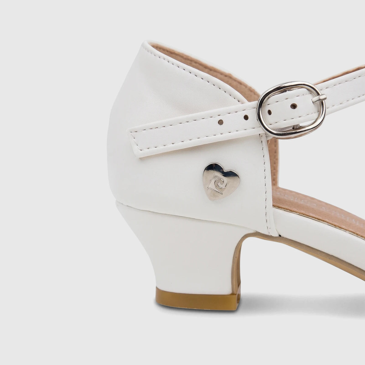 Close-up of a white PC Girls Dress Heel shoe, featuring an ankle strap with a silver buckle and a heart emblem.