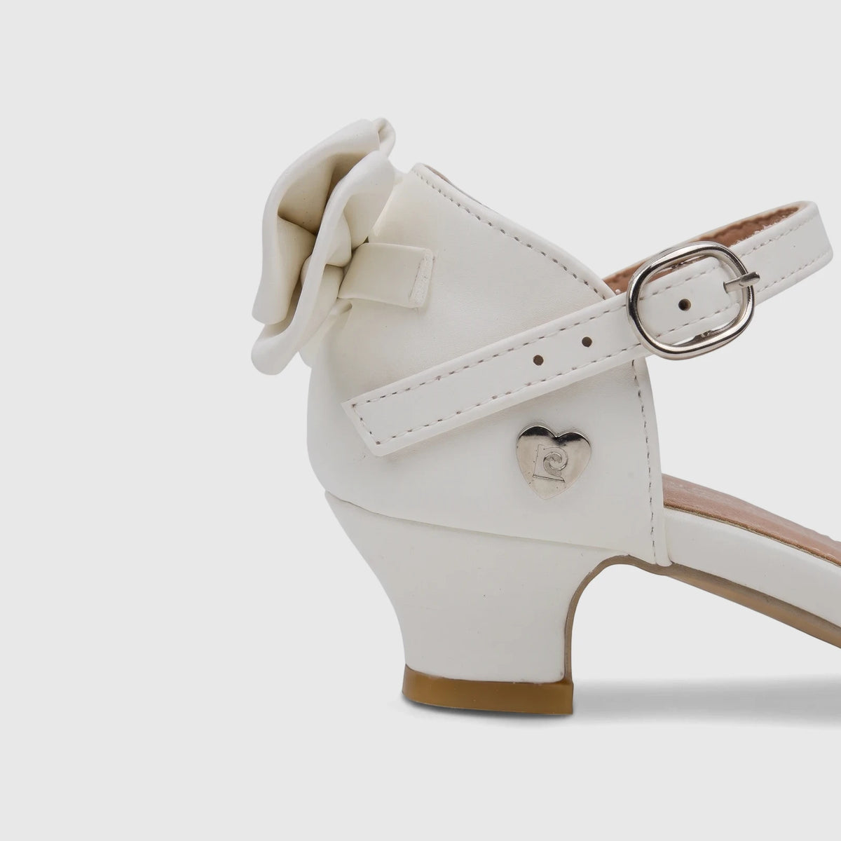 White PC girls' dress heel shoe with a bow, silver buckle on the ankle strap, and a heart emblem, viewed from the side.