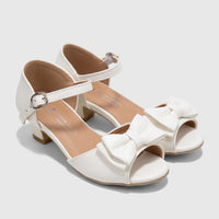 A pair of white Pierre Cardin girls' dress heels with bows and ankle straps, seen from an elevated angle.