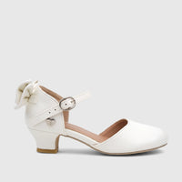White girls' dress heel with an elegant bow detail, ankle strap with silver buckle and heart charm, side view.