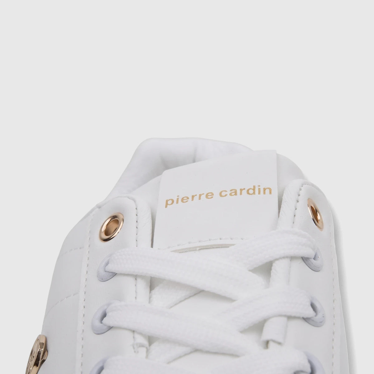 Close-up of a white Pierre Cardin PCL11006 casual sneaker with golden eyelets and the brand logo on the tongue.