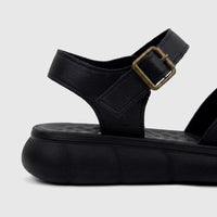 Close-up of a black PC Ladies Comfort Sandal with a platform sole and a bronze buckle on the ankle strap.