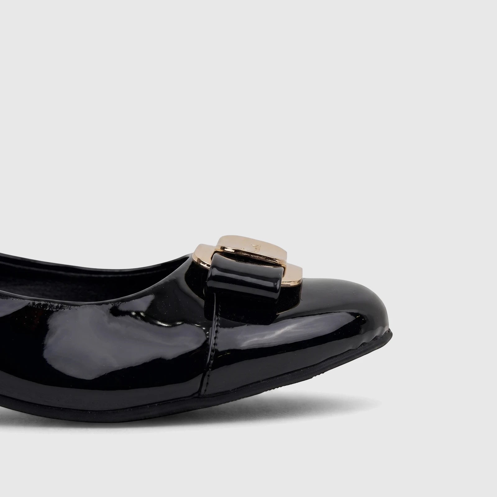 Close-up of a shiny black patent leather ladies dress court shoe with an elegant golden buckle on the vamp.