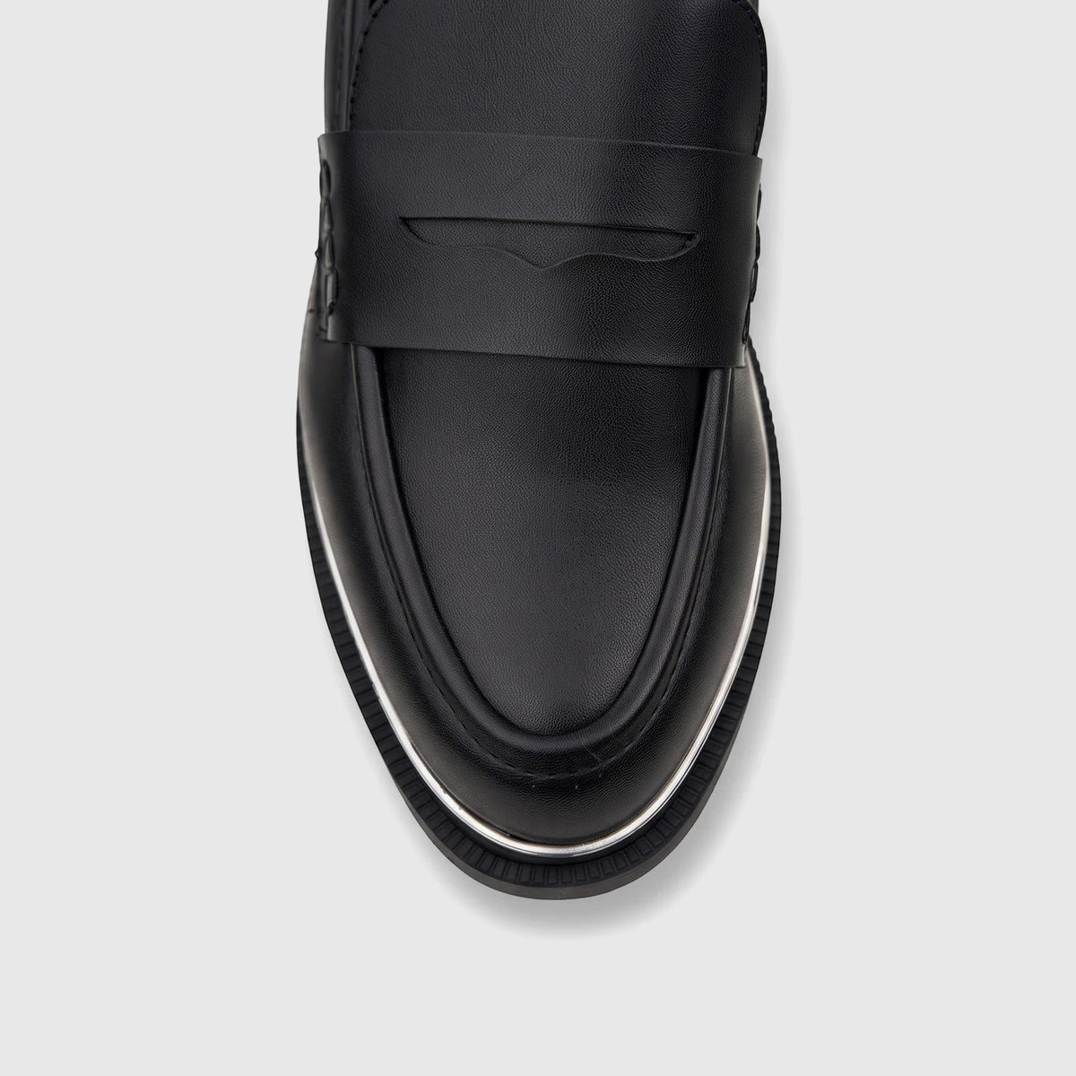 Close-up of a black leather women's dress loafer with a penny strap detail and white sole trim, viewed from above.