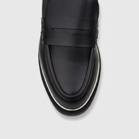 Close-up of a black leather women's dress loafer with a penny strap detail and white sole trim, viewed from above.