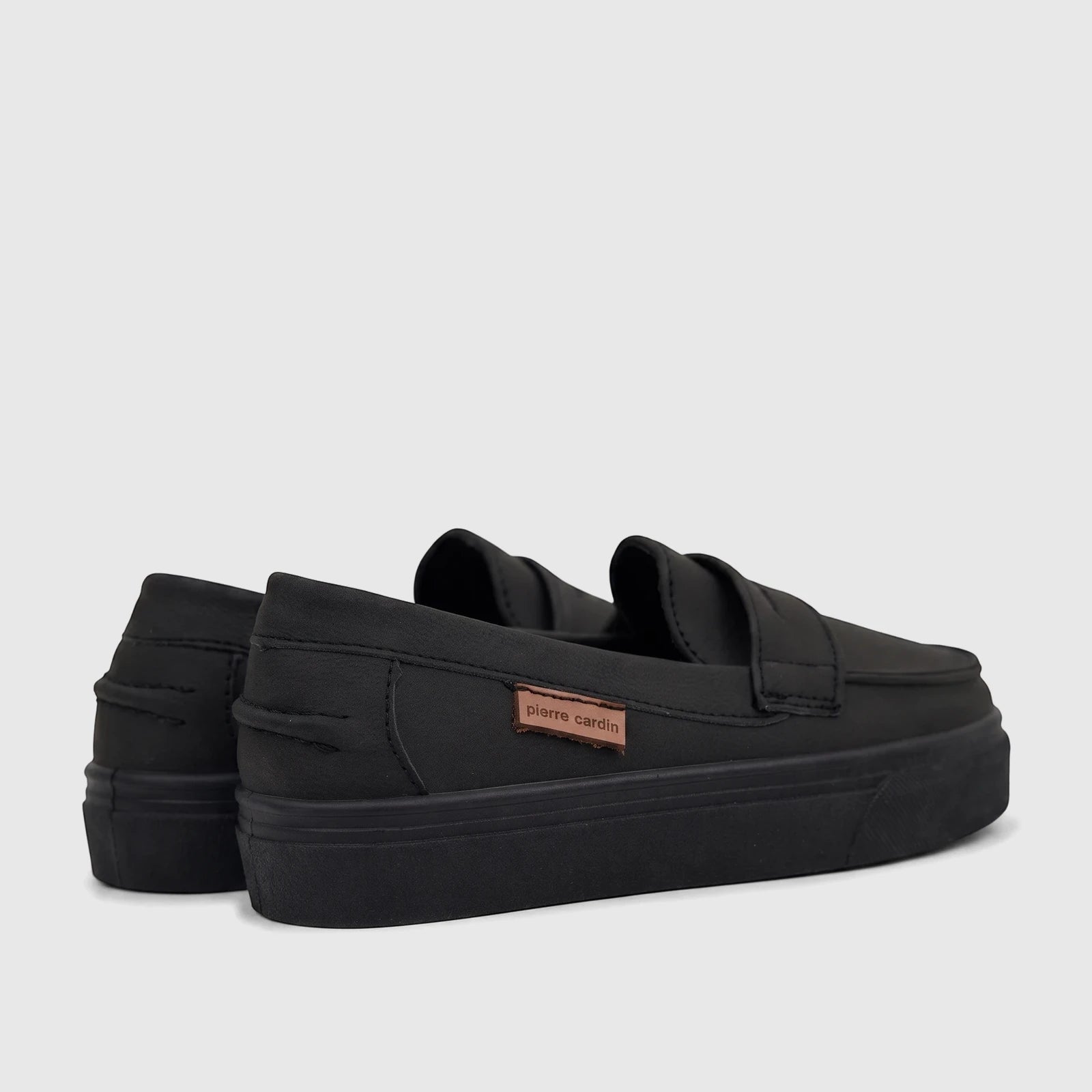 Pair of black Pierre Cardin boys casual slip-on shoes with platform soles, viewed from a rear-side angle on a white