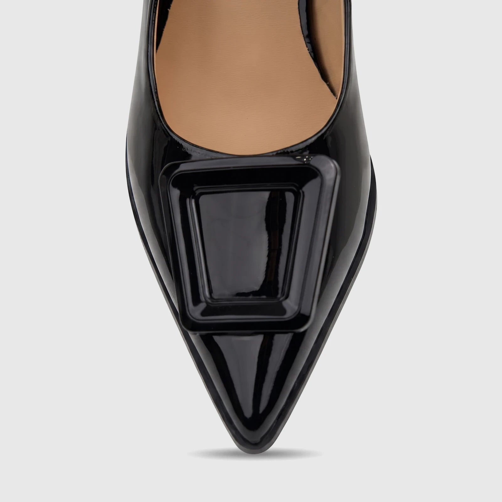 Close-up of a glossy black patent leather pointed-toe high-heeled shoe with a prominent square buckle on the vamp, viewed