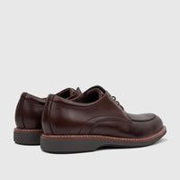A pair of dark brown Rockport Men's Dress/Comfort Lace Up Leonard shoes from a side view, showing white stitching detail and