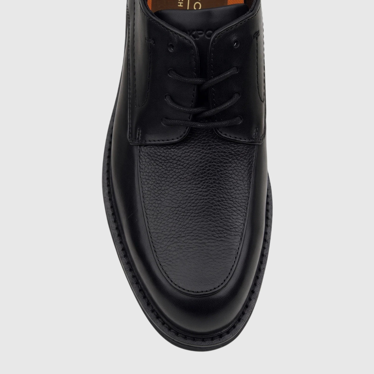 Black Rockport men's lace-up dress shoe with smooth and textured leather, seen from a top-down perspective on a white