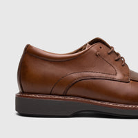 Close-up of a Rockport Men's Leonard British Tan lace-up dress shoe, showcasing the rich brown leather and detailed