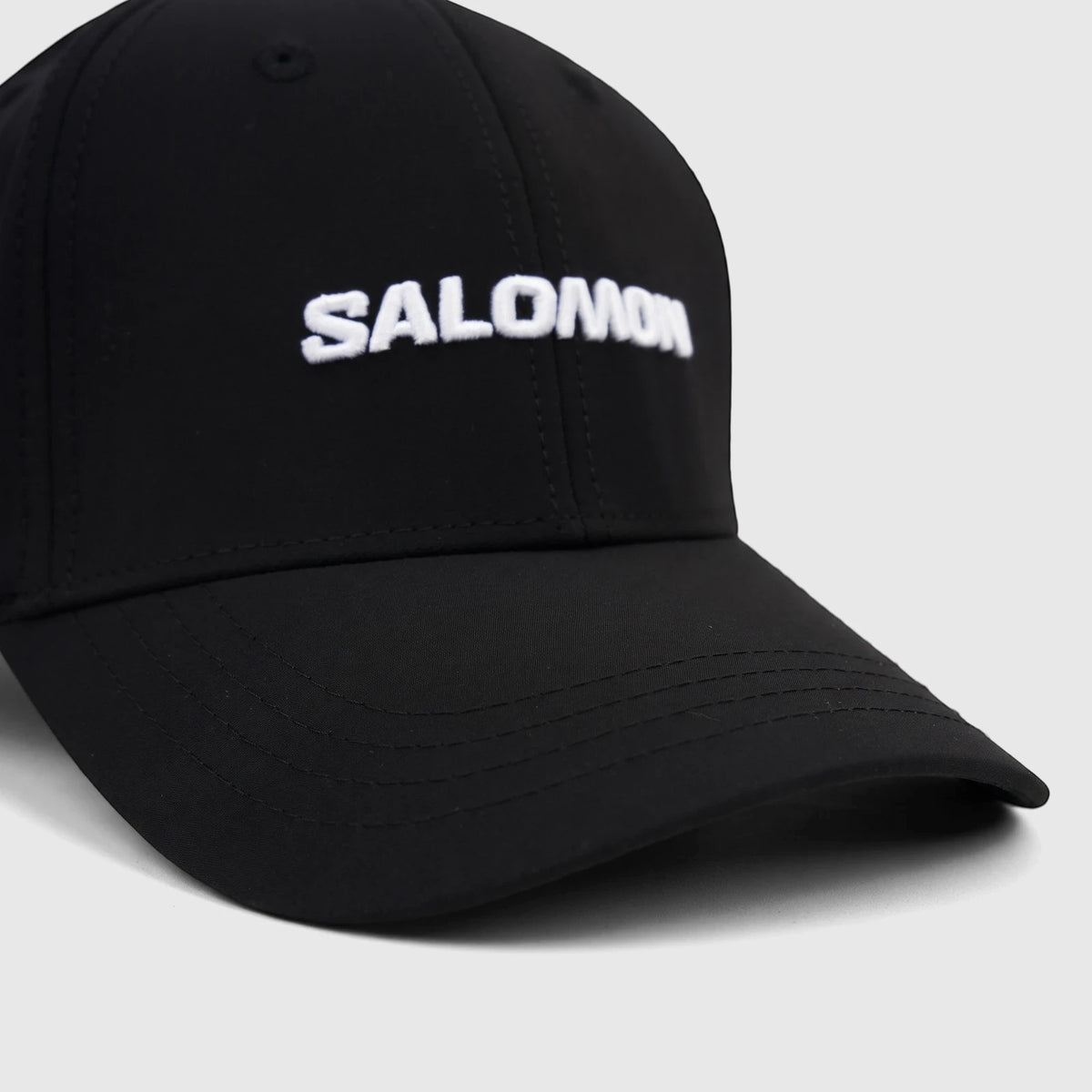 Close-up of a deep black Salomon adjustable cap with a white embroidered Salomon logo on the front, viewed from an angle.