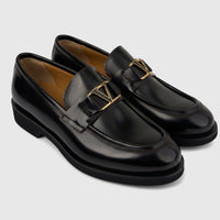 Pair of Valentino men's black leather slip-on loafers with chunky soles and gold-tone V-logo hardware, shown from an