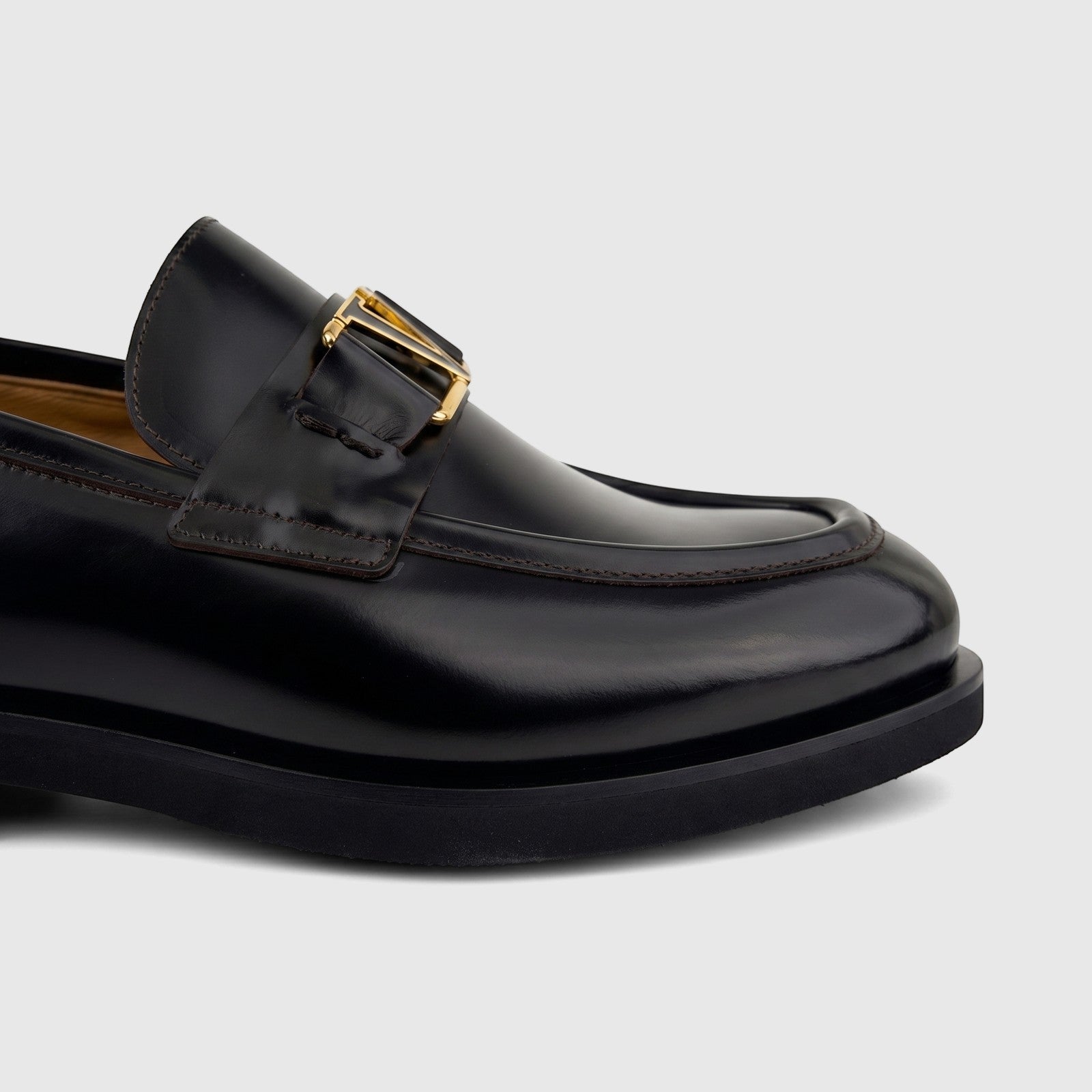 Close-up of a men's black leather Valentino slip-on loafer with a chunky sole and gold-tone 'V' logo hardware.