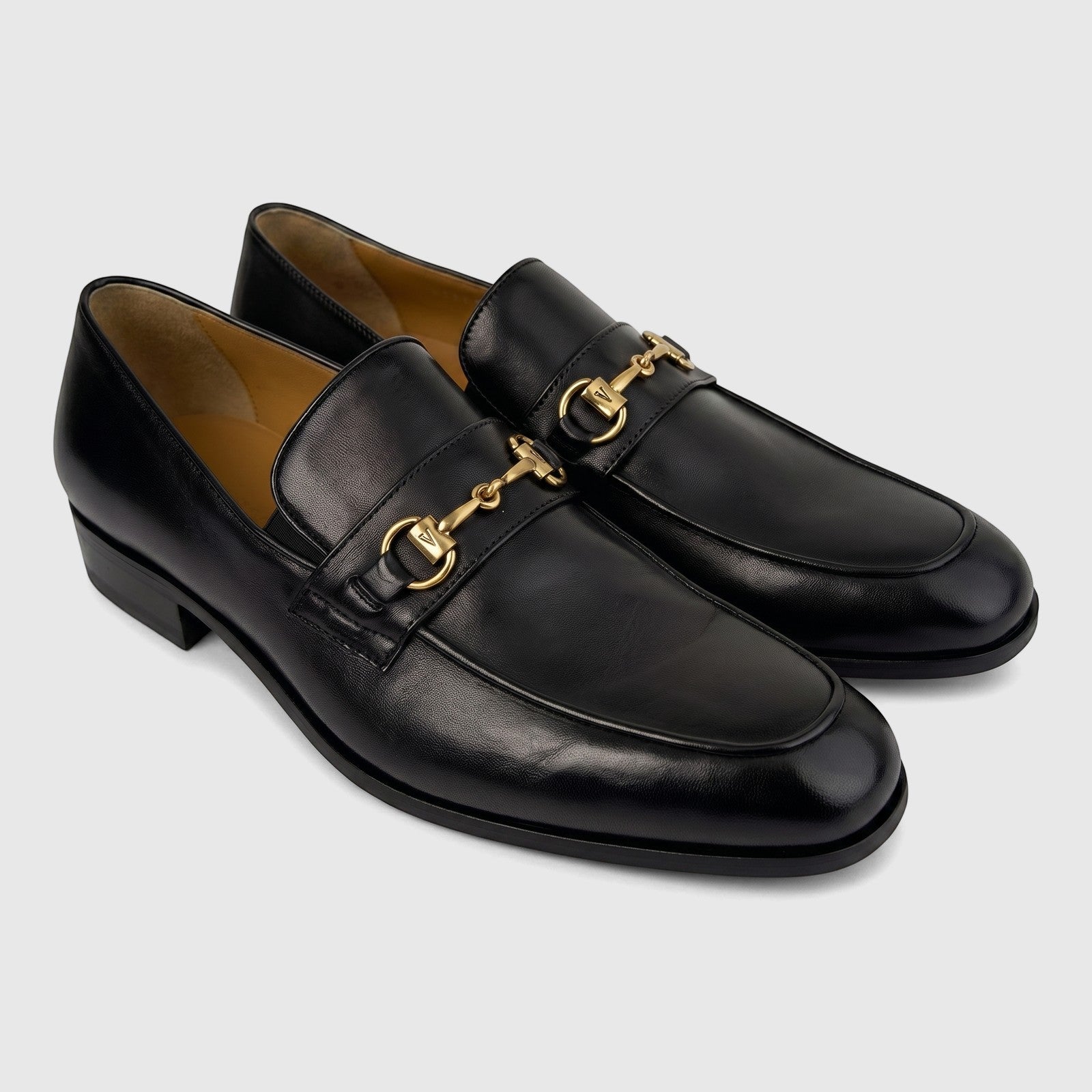Valentino Men's Black Leather Dress Slip-On Shoes, featuring prominent gold-tone horsebit hardware with a 'V' logo, in a