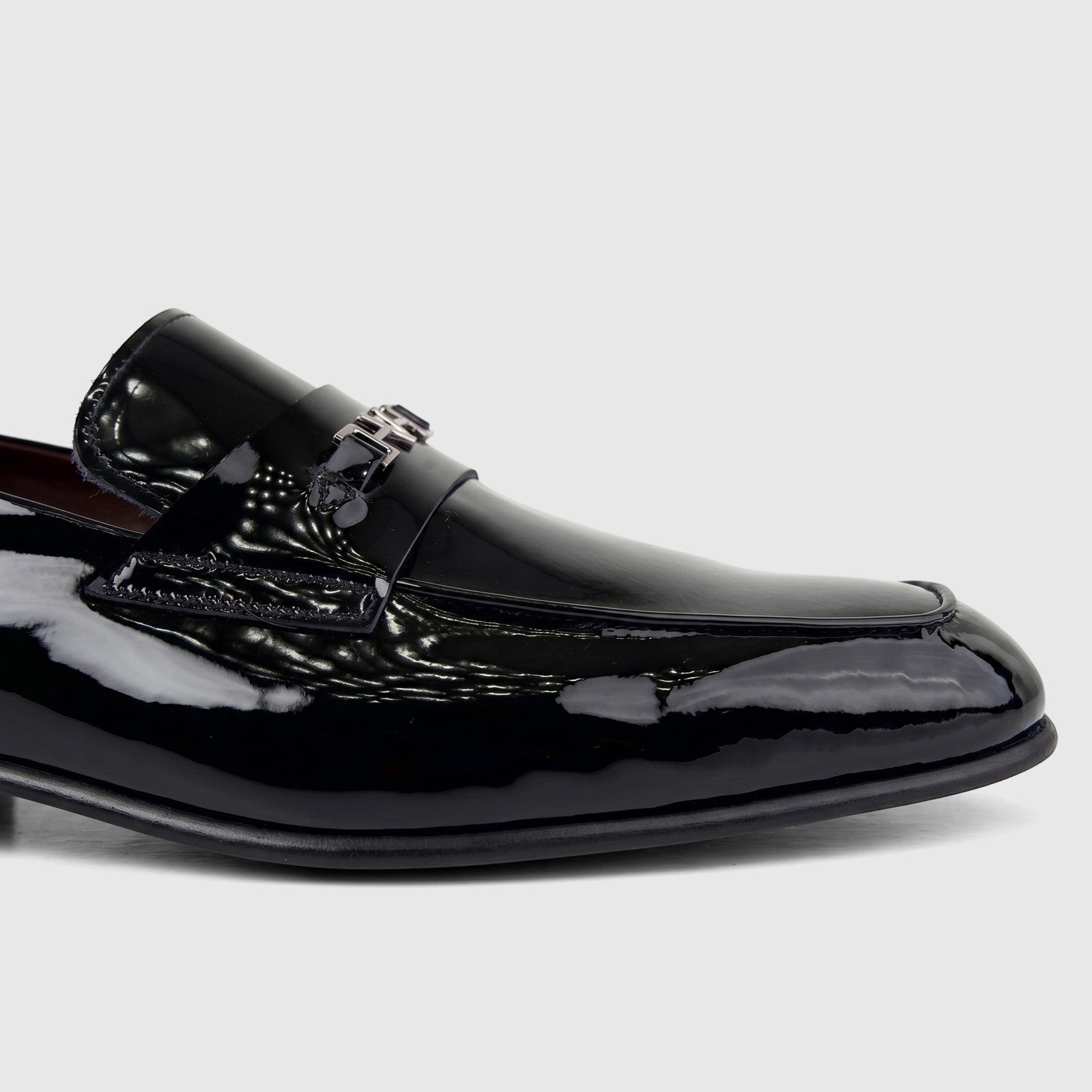 Valentino Men's Black Patent Leather Dress Slip On loafer, shown from a side view, featuring a glossy finish and metal
