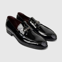 A luxurious pair of men's black patent leather slip-on dress shoes, featuring sleek design and silver-tone hardware accents.