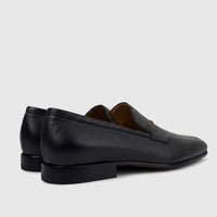 Valentino Men's black pebbled leather dress slip-on shoes with red soles, viewed from a rear side angle.