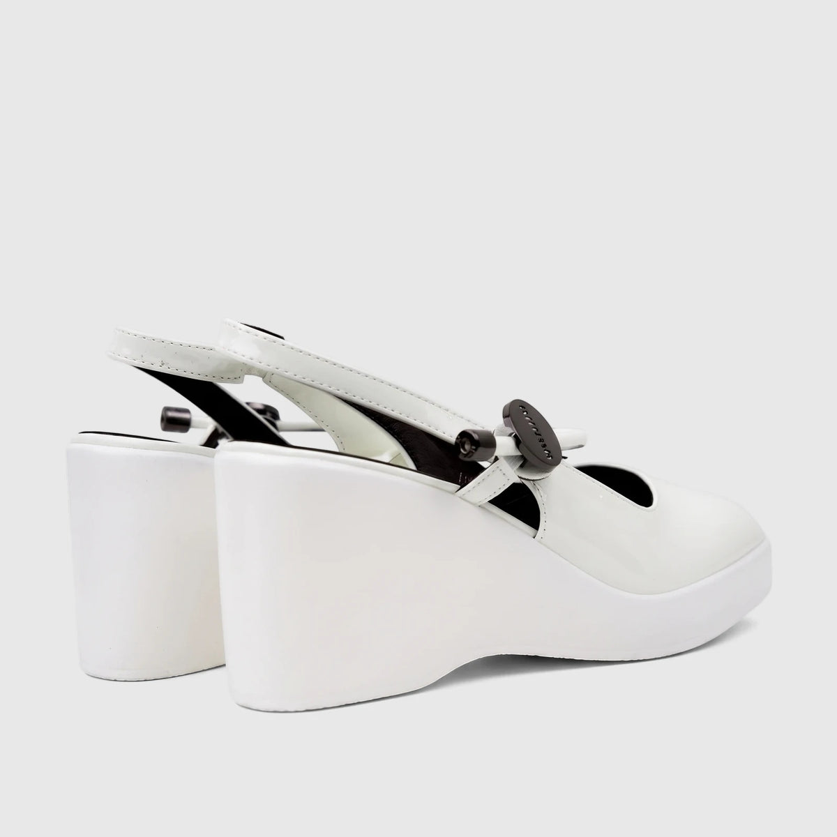 White patent leather wedge sandals with slingback strap and decorative black buckle, side view.