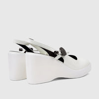 White patent leather wedge sandals with slingback strap and decorative black buckle, side view.